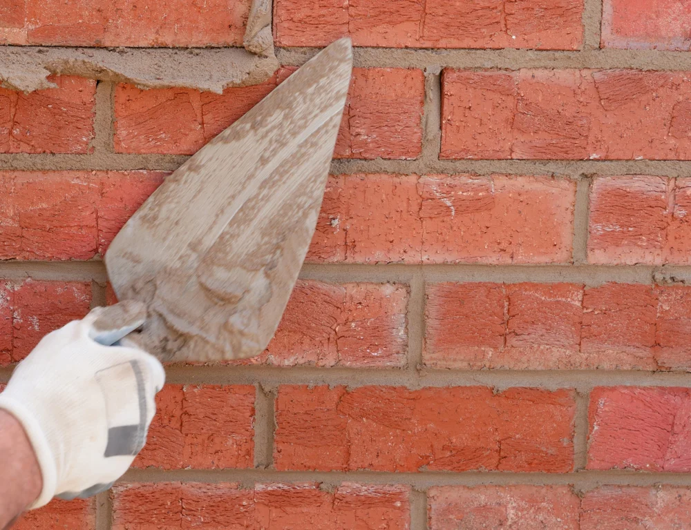 Close up of hand and trowel repointing a brick wall.